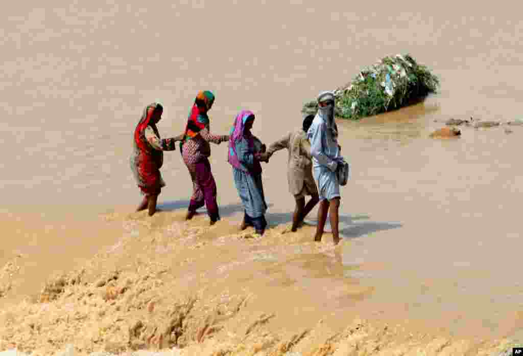 Pakistani family members help each other cross a stream caused by heavy rainfall in Karachi.