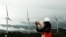FILE - A woman takes pictures of wind power plant propeller blades in Sidenreng Rappang, Sulawesi Island, Indonesia, Jan. 15, 2018. 