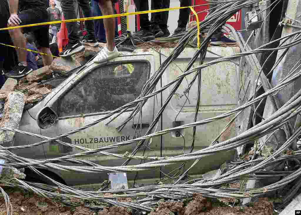 People stand on top of a damaged car at the scene of a missile strike in the southern suburbs of Beirut, Lebanon.