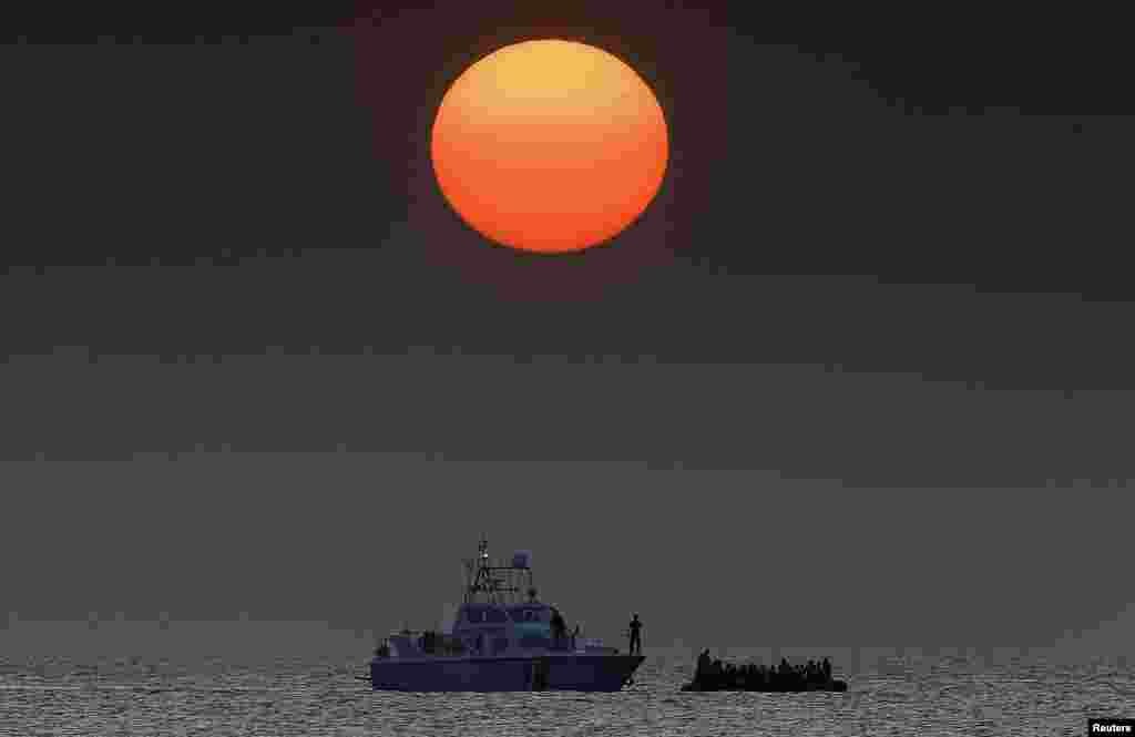 An officer onboard a Greek Coast Guard boat (L) talks to Syrian refugees overcrowding a dinghy as it drifts in the Aegean Sea between Turkey and Greece after its motor broke down off the Greek island of Kos.