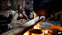 In this Nov. 15, 2018, photo, Mashpee Wampanoag Kerri Helme, of Fairhaven, Mass., uses plant fiber to weave a basket while sitting next to a fire at the Wampanoag Homesite at Plimoth Plantation, in Plymouth, Mass. 