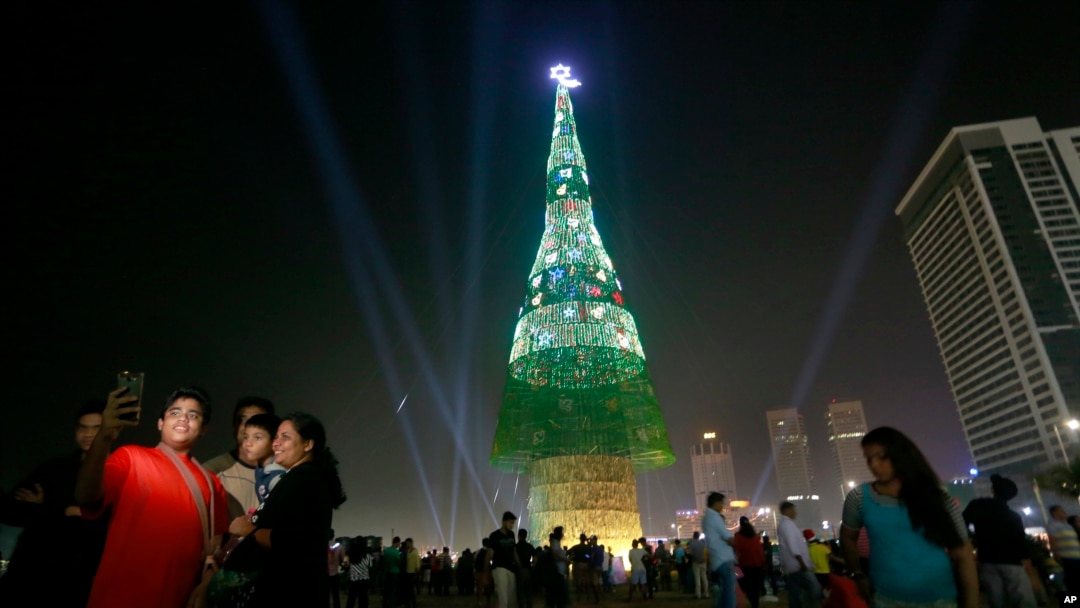 A Sri Lankan family takes photographs standing near an enormous artificial Christmas tree as others gather in Colombo, Sri Lanka, Dec. 24, 2016. Sri Lanka has unveiled a towering Christmas tree, claiming to have surpassed the world record for the tallest 