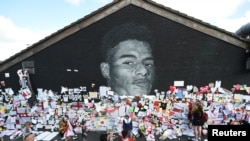FILE - People look at messages of support on the Marcus Rashford mural after it was defaced following the Euro 2020 Final between Italy and England, in Withington, Manchester, Britain, July 13, 2021. Players also were targets of online abuse.