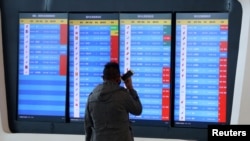 FILE - A man stands in front of a screen showing that multiple departure flights have been cancelled following the outbreak of the coronavirus, at an airport in Wuhan, Hubei province, China, Jan. 23, 2020. 