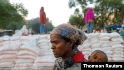 FILE - A woman carries an infant as she waits in line for food, at the Tsehaye primary school, which was turned into a temporary shelter for people displaced by conflict, in the town of Shire, Tigray region, Ethiopia, March 15, 2021.
