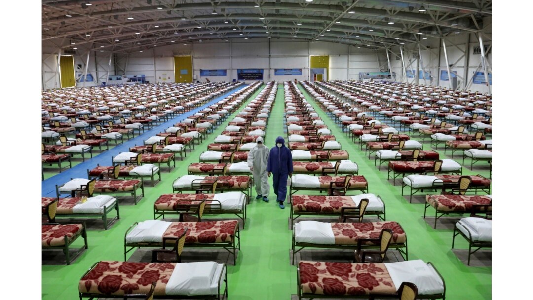 Men in protective gear walk past rows of beds at a temporary 2,000-bed hospital for coronavirus patients set up by the Iranian army, at an exhibition center in northern Tehran, Iran, March 26, 2020.