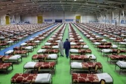 Men in protective gear walk past rows of beds at a temporary 2,000-bed hospital for coronavirus patients set up by the Iranian army, at an exhibition center in northern Tehran, Iran, March 26, 2020.