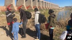 Un contrabandista mexicano guía a una familia haitiana a través de la presa Morelos sobre el río Colorado desde Los Algodones, México, el viernes 4 de febrero de 2022, hasta Yuma, Arizona, en el otro lado. 