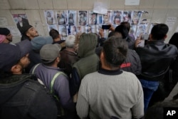 People examine photos as they search for missing or deceased people on the wall outside the morgue of Al-Mojtahed Hospital in Damascus, Syria, Dec. 11, 2024.