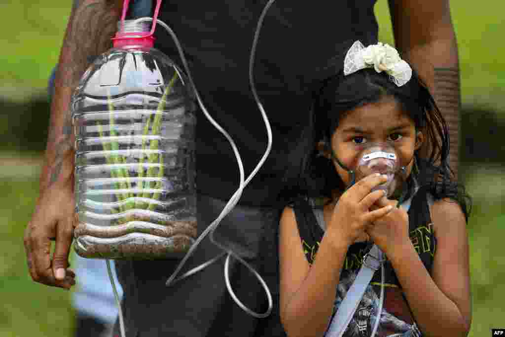 스리랑카 콜롬보에서 열린 삼림 보호와 기후 변화 대응 촉구 집회에서 한 소녀가 식물이 담긴 플라스틱병이 연결된 마스크를 쓰고 있다.