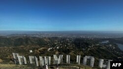 FILE - In this May 24, 2020, photo, a family wearing face masks hike at Griffith Park at the back of the Hollywood sign during the novel coronavirus pandemic in Los Angeles, California.