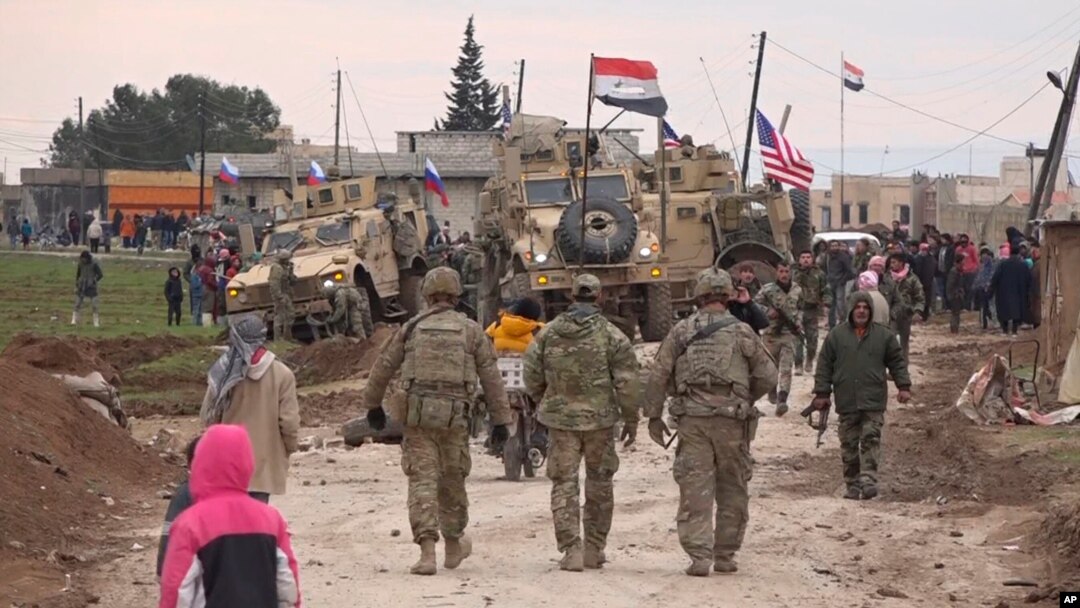 FILE - In this frame grab from video, Russians, Syrians and others gather next to an American military convoy stuck in the village of Khirbet Ammu, east of Qamishli city, Syria, Feb. 12, 2020. 