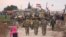 In this frame grab from video, Russian, Syrian and others gather next to an American military convoy stuck in the village of Khirbet Ammu, east of Qamishli city, Syria, Feb. 12, 2020. 
