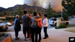 Una familia se conforta luego de evacuar su casa mientras los bomberos combaten las llamas en Azusa, California.