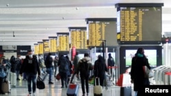 People walk carrying their luggage past train schedule displays at Termini train station, on the day the government lays out a plan of coronavirus disease (COVID-19) restrictions over the Christmas period, in Rome, Dec. 19, 2020.