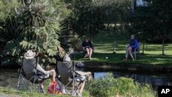 FILE - Neighbors chat across a stream as they practice social distancing in a suburb of Christchurch, New Zealand, Apr. 5, 2020. 