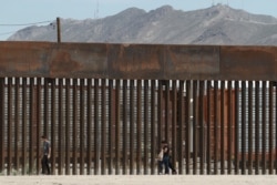 FILE - People walk along a border wall in El Paso, Texas, July 17, 2019.