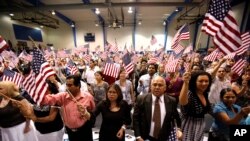 FILE - People hold flags as they are sworn in as U.S. citizens during a naturalization ceremony in Phoenix, Arizona.