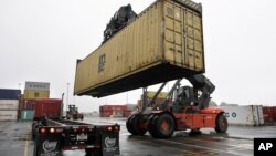 In this photo taken December 18, 2012, a reach stacker operated by a longshoreman (R) places a shipping container on a tractor trailer truck at the Port of Boston, Massachussets.