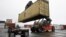 In this photo taken December 18, 2012, a reach stacker operated by a longshoreman (R) places a shipping container on a tractor trailer truck at the Port of Boston, Massachussets.
