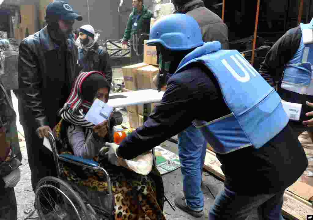 This photo released by the Syrian official news agency SANA shows a U.N. relief worker giving food supplies to a Palestinian woman in a wheelchair at the gate of the besieged Yarmouk refugee camp on the southern edge of Damascus, Feb. 4, 2014. 