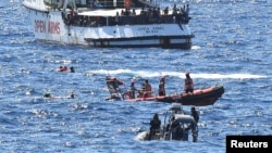 FILE - Migrants swim after jumping off the Spanish rescue ship Open Arms, close to the Italian shore in Lampedusa, Italy, Aug. 20, 2019.
