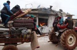 Displaced Syrians pass a house still on fire as they flee shelling on the town of Abyan, in the western rebel-held part of the northern Syrian province of Aleppo, near the border with Turkey, Feb. 12, 2020.