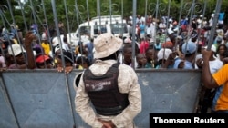 A national police officer stands guard as people affected by the Aug. 14 earthquake wait for food provided by the World Food Program, at a school in Port Salut, Haiti, Aug. 24, 2021. 