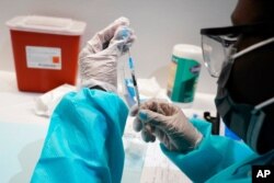 FILE- A health care worker fills a syringe with the Pfizer COVID-19 vaccine, at the American Museum of Natural History in New York, July 22, 2021.