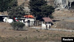 Uniformed men walk near a building with Syrian and Ba'ath Party flags in Quneitra, on the Syrian side of the cease-fire line between Israel and Syria, as seen from the Israeli-occupied Golan Heights, July 26, 2018.