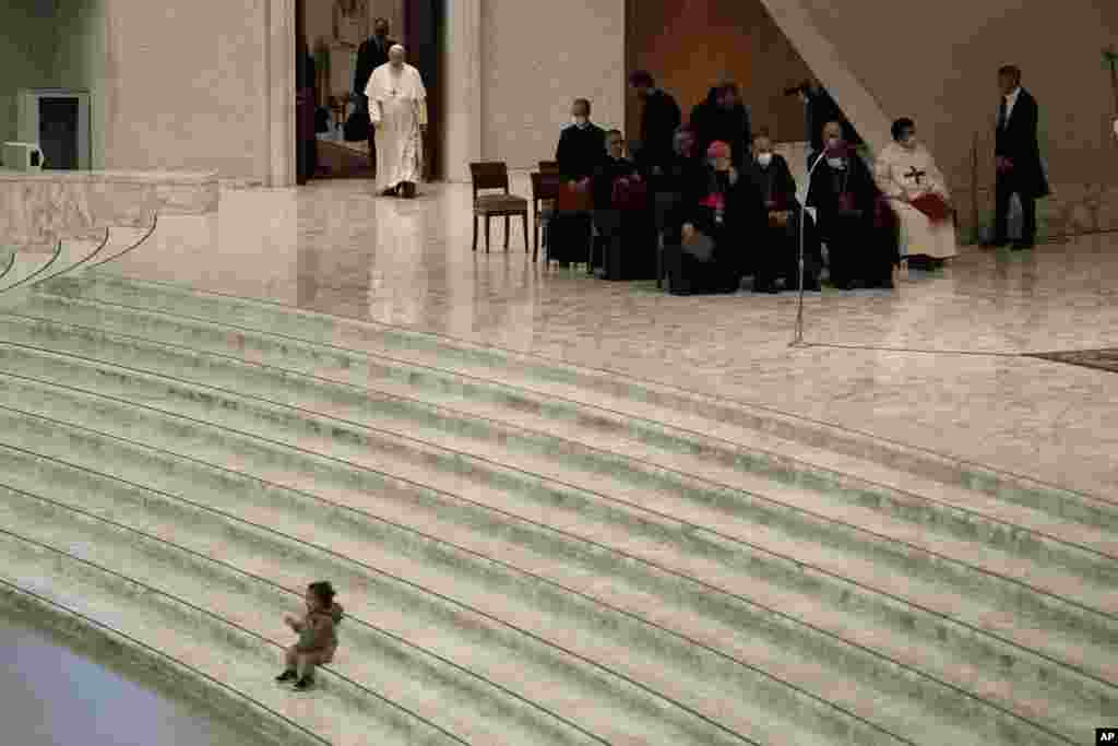 Pope Francis arrives for his weekly general audience as a child plays on the steps of the Paul VI Hall, at the Vatican.