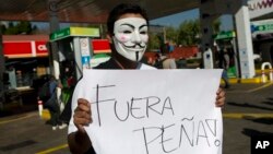 A masked protester holds a sign that says "Pena Out!" as people angry over hiked gas prices under President Enrique Pena Nieto's government block for hours one of the city's oldest gas stations at a main intersection in Mexico City, Jan. 2, 2017.