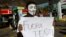 A masked protester holds a sign that says "Pena Out!" as people angry over hiked gas prices under President Enrique Pena Nieto's government block for hours one of the city's oldest gas stations at a main intersection in Mexico City, Jan. 2, 2017.