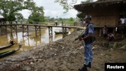 FILE - A Myanmar border guard police officer stands guard in Taung Bazar village, Buthidaung township, northern Rakhine state, Myanmar, July 13, 2017.