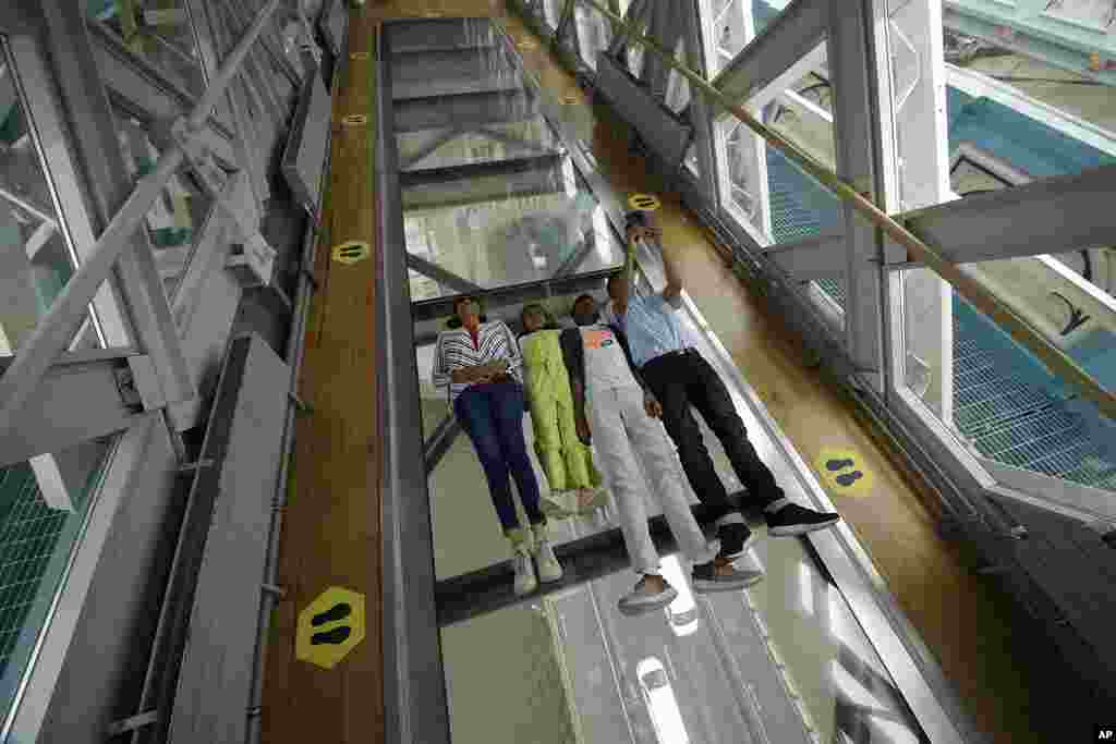 Visitors pose for photographs on the glass walkway at the Tower Bridge Visitor Attraction, in London, on the first day it was allowed to reopen as the British government relaxes its third coronavirus lockdown restrictions.