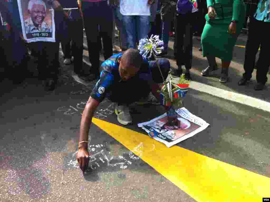 Un chico escribe un saludo a Mandela sobre el pavimento de la calle. [Foto: Celia Mendoza, VOA].