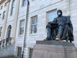 Patung John Harvard di Universitas Harvard, objek wisata populer di kampus di Cambridge, Massachusetts, didekorasi dengan topeng pelindung, 14 Maret 2020. (Foto: AP)