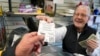 (ARCHIVO) Dot Skoko, propietario de la tienda Dot's Dollar More or Less en Mt. Lebanon, Pensilvania, le entrega a un cliente un billete de lotería Mega Millions, el jueves 5 de enero de 2022.