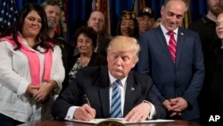 President Donald Trump, accompanied by Veterans Affairs Secretary David Shulkin, center right, and veterans, signs an Executive Order on "Improving Accountability and Whistleblower Protection" at the Department of Veterans Affairs in Washington, April 27, 2017. 