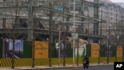 A delivery rider passes by workers laboring at a new residential building under construction in Beijing on March 1, 2025.