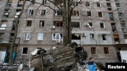 FILE PHOTO: A boy stands next to a wrecked vehicle in front of a damaged apartment building in Mariupol