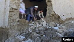 阿富汗楠格哈尔省灾区的一名男子和他的儿子清理在地震中毁坏的房屋。（2015年10月27日）