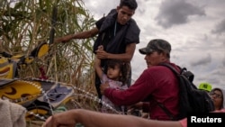 Una niña migrante venezolana es asistida por compatriotas mientras intentan pasar entre alambres de púas colocados a lo largo de las orillas del río Grande, en Eagle Pass, EEUU, el 6 de octubre de 2023.