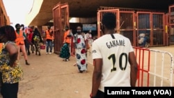 Des commerçants qui doivent passer les contrôles sous les regards des volontaires, des hommes en gilets orange, à Ouagadougou, le 24 avril 2020. (VOA/Lamine Traoré)