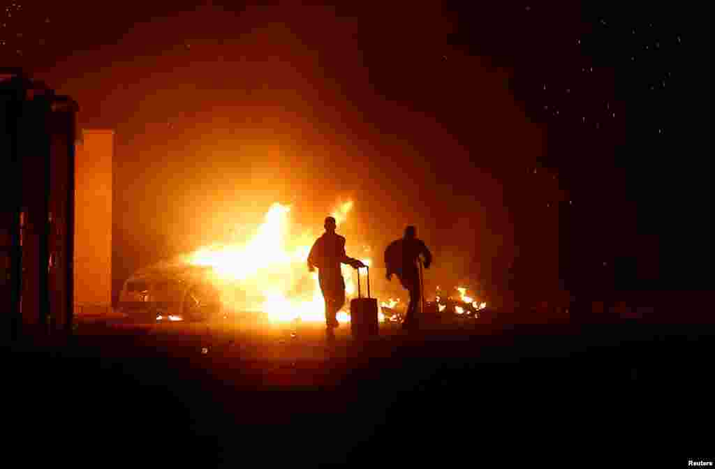 People run while a vehicle is burning, during riots at the Hal Far Open Center migrant camp in Hal Far, Malta, Oct. 21, 2019.