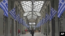 Pedestrian walk inside an arcade full of Greek flags in central Athens, on Wednesday, March 14, 2012. 