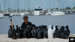 Žena pun i vreće peskom na plaži u Tampi, kako bi se zaštitila od poplava (Foto: AP/Julio Cortez)