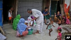 A Rohingya refugee distributes wheat, donated by locals, among other refugees at a camp for the refugees in New Delhi, India. 