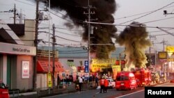 Firefighters gather around black smoke spewing from an unmanned underground cable facility in Niiza, Saitama prefecture on October 12, 2016. TEPCO said smoke was detected at its unmanned power substation in Niiza city, near Tokyo, and officials are looking into whether it's related to the blackout.