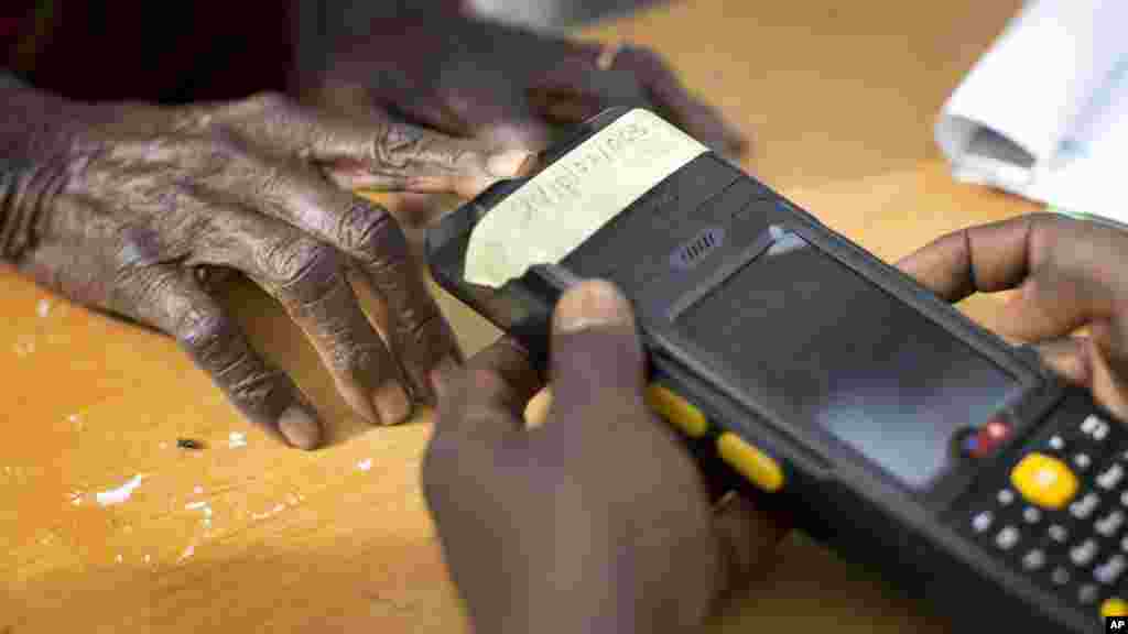 An elderly Nigerian woman validates her voting card using a fingerprint reader, prior to casting her vote later in the day, in the home town of opposition candidate Gen. Muhammadu Buhari, in Daura, Nigeria, March 28, 2015. 